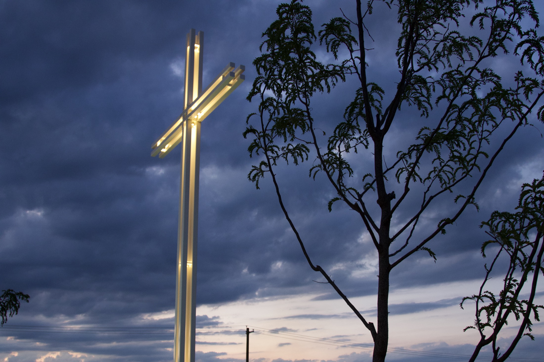 A cross rising above bare winter trees at dusk.