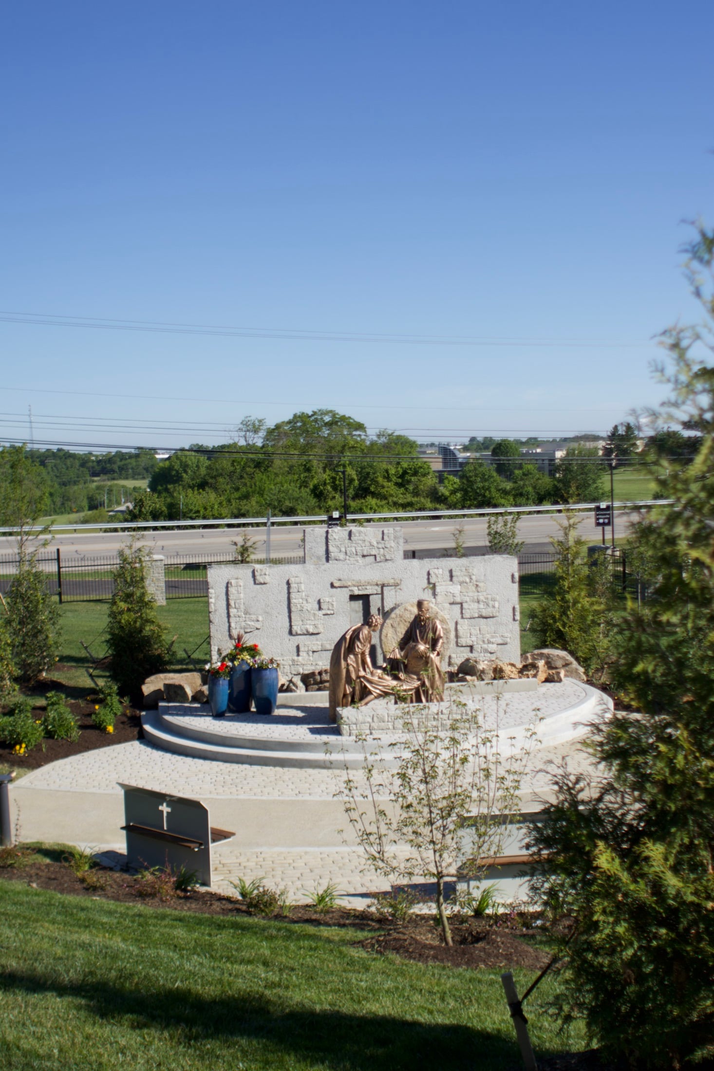 A wide view of the grounds, showing a curved stone gathering area, benches, and the surrounding countryside.