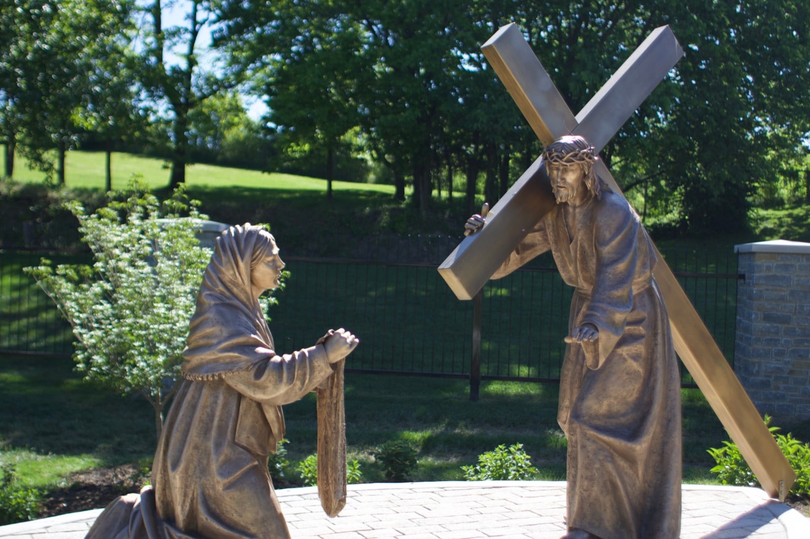 A bronze figure of Veronica kneeling before Christ on the garden path at dusk.
