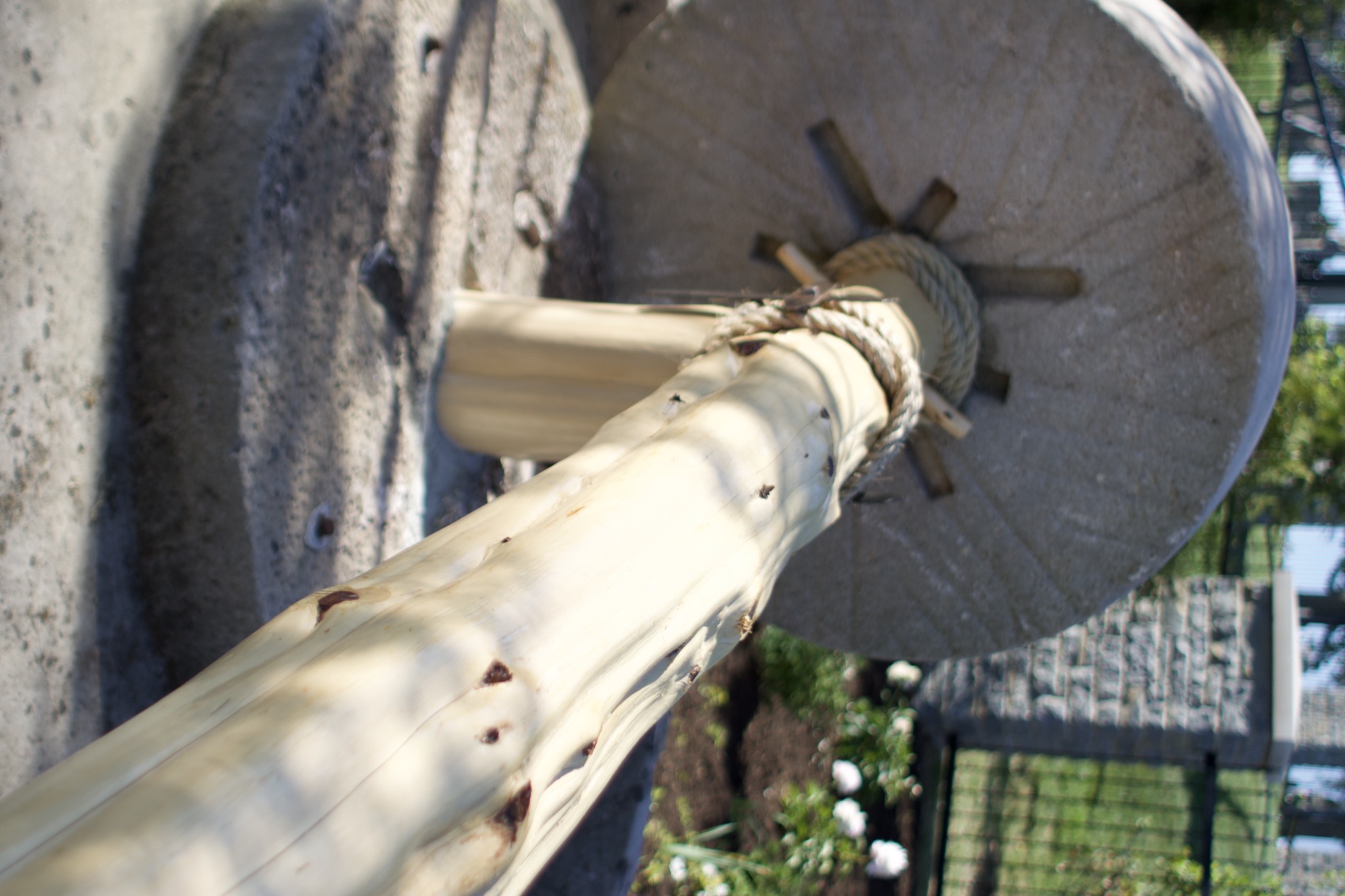 A stone olive press wheel and wooden beam, part of the Gethsemane Gardens installation near the entrance to the path.