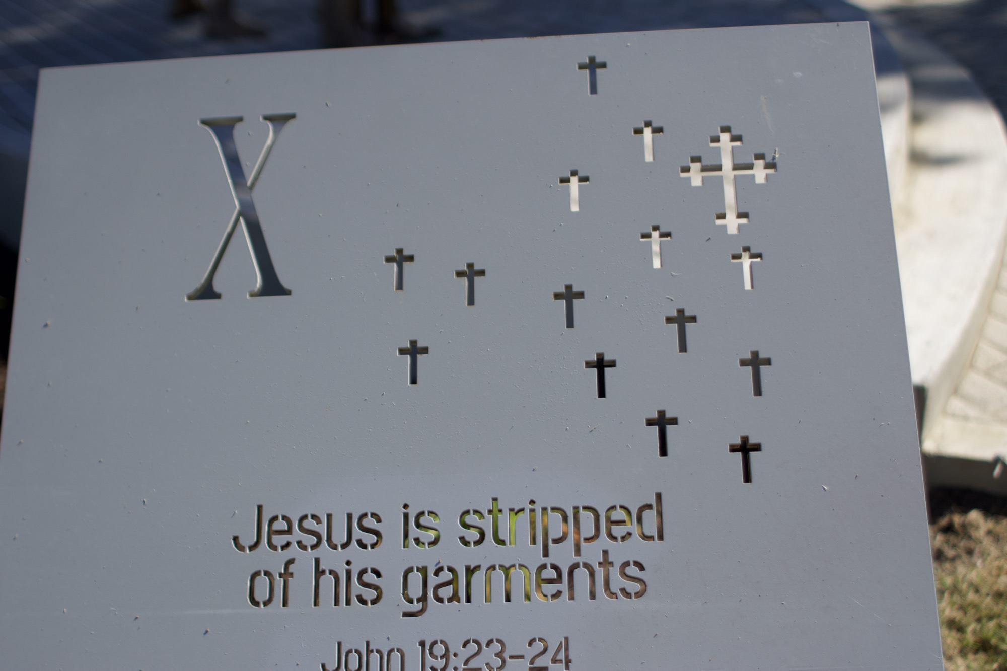 A carved station marker reading Jesus is stripped of his garments, with small cross cutouts.