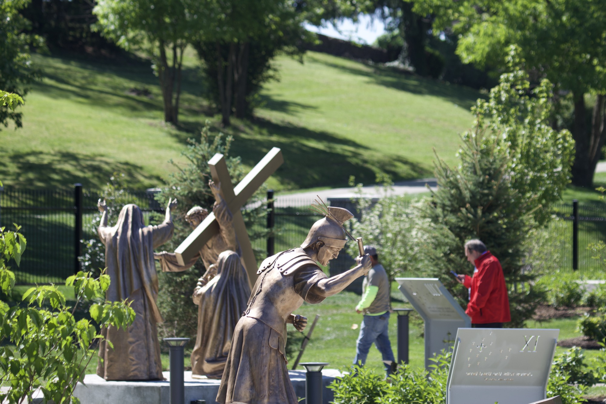 Bronze figures of a Roman soldier raising the cross as two women look on, garden setting.