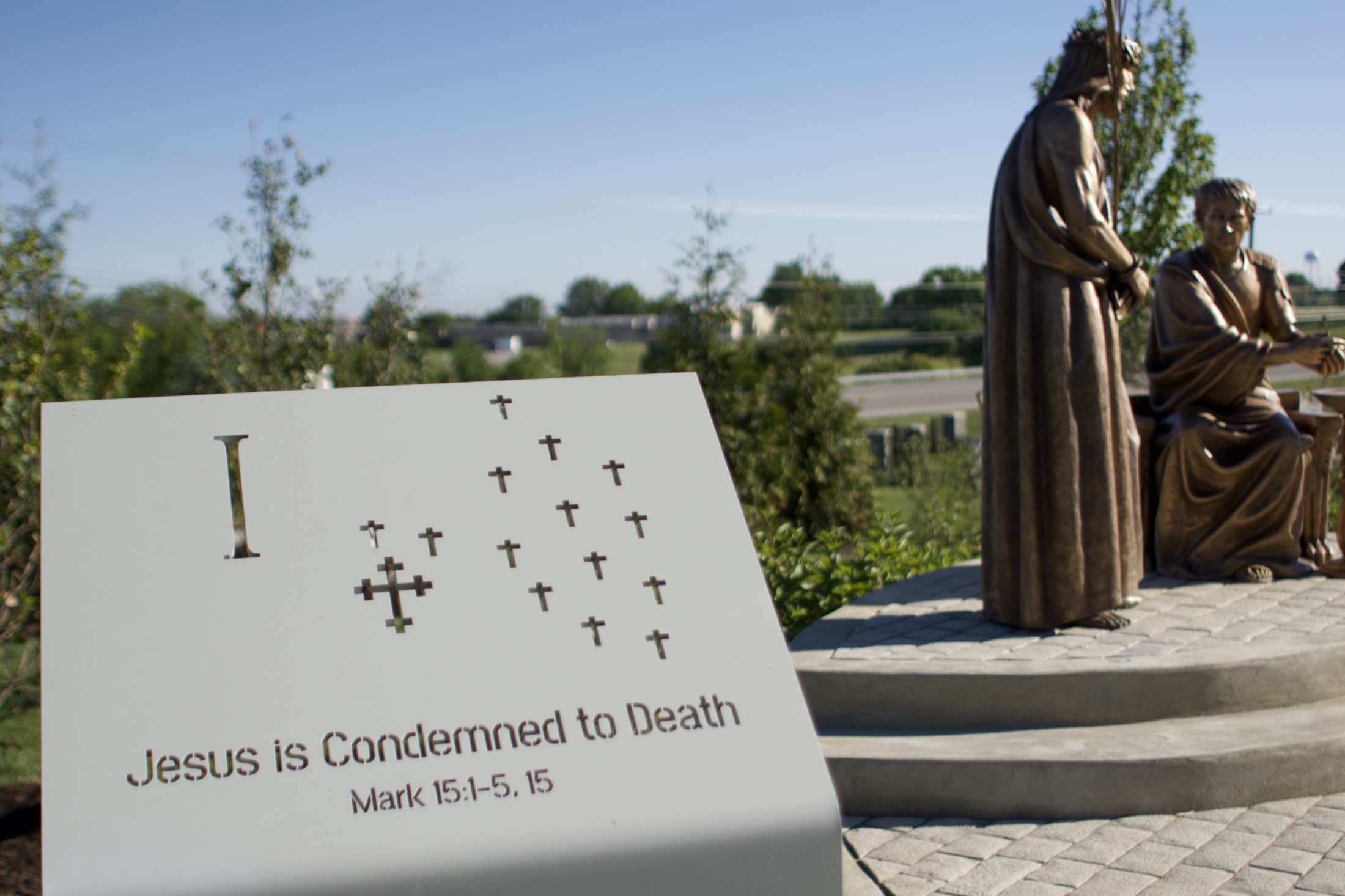 A carved stone station marker with a scripture citation and raised braille dots.
