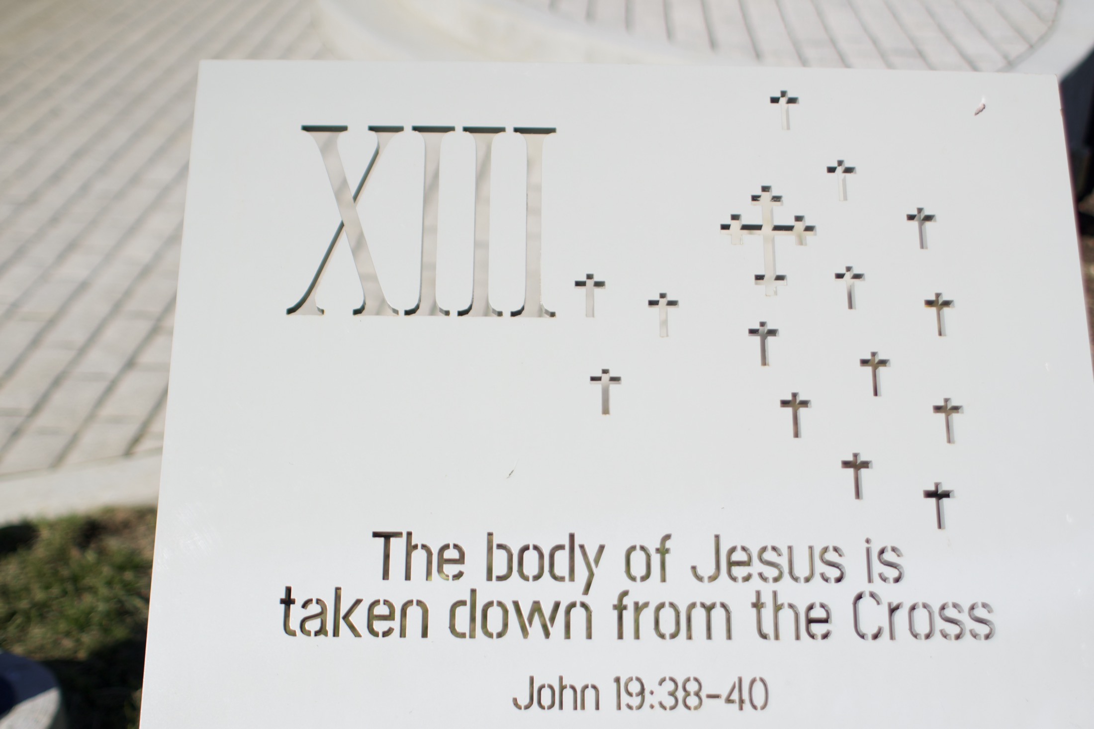 A carved stone station marker for Station XIII, inscribed with scripture and raised braille dots.