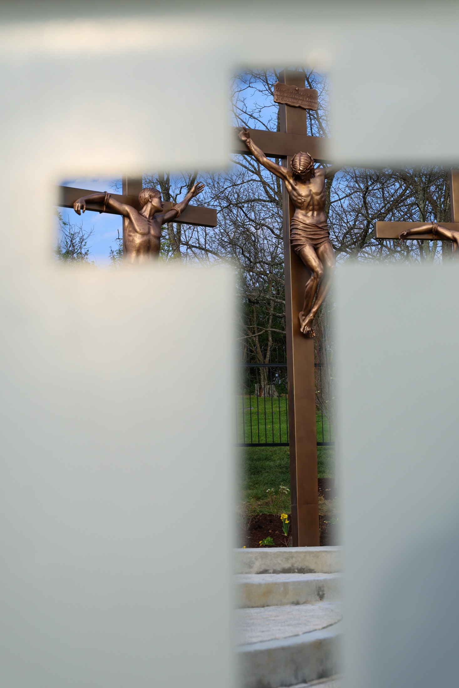 The three crosses of the crucifixion scene, seen through a decorative stone screen, bare winter trees beyond.